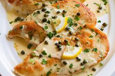 two pieces of chicken covered in white sauce and garnished with lemon slices on a plate