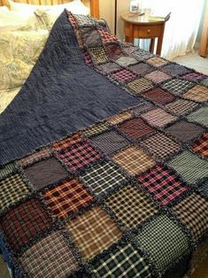 a bed covered in a blue blanket with brown and black plaid squares on it, next to a night stand