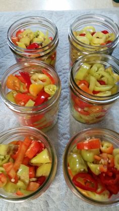 six glass jars filled with sliced vegetables on a white table cloth next to a knife and fork