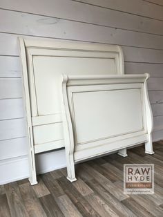 a white bed frame against the wall in a room with wood flooring and walls