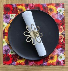 a black plate topped with a white napkin on top of a flowered place mat