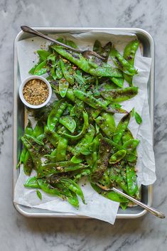 a tray filled with green beans and seasoning on top of a marble countertop