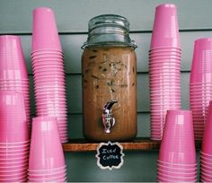 there is a mason jar with coffee in it surrounded by pink cups on the shelf