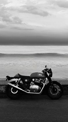 a black and white photo of a motorcycle parked on the side of the road next to the ocean