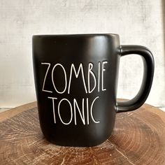 a black coffee mug with the words zombie tonic on it sitting on top of a tree stump