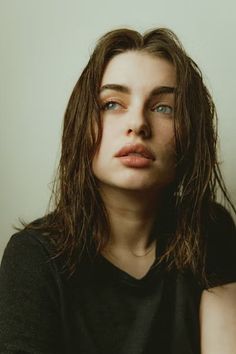 a woman with long hair and blue eyes posing for a photo in front of a white wall