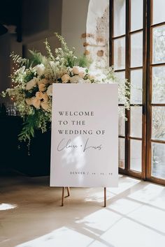 a welcome sign sitting on top of a wooden easel next to a bouquet of flowers