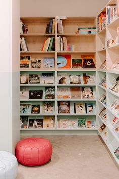 a room filled with lots of books on shelves next to a red ball and ottoman