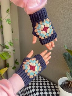 two hands with crocheted gloves on top of a table next to a potted plant