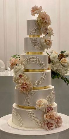 a three tiered wedding cake with flowers on the top and bottom, sitting on a table