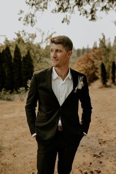 a man in a tuxedo standing on a dirt road with his hands in his pockets