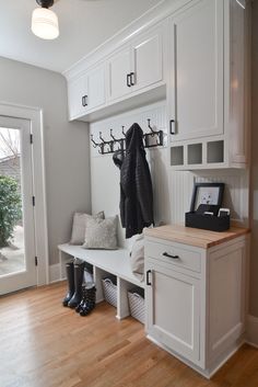 a coat rack and bench in a white entryway with wood flooring next to an open door