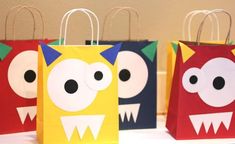 three paper bags decorated with monster faces and mouths, all lined up on a table