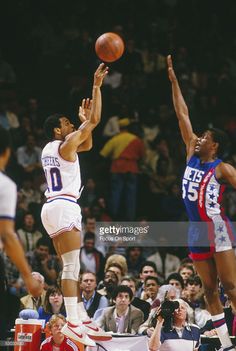 two men playing basketball in front of an audience at a sporting event, one is jumping up for the ball