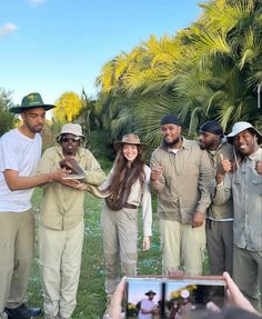 a group of people standing next to each other on a lush green field with palm trees in the background