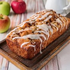 a loaf of cinnamon apple bread with icing on a cutting board next to apples