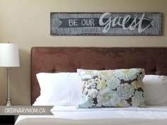 a bedroom with a bed, lamp and sign on the wall above it that says be our guest