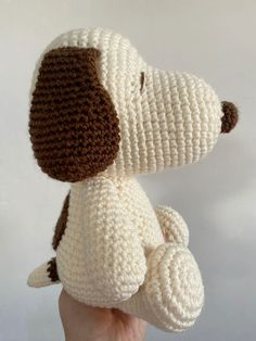 a hand holding a crocheted white and brown dog stuffed animal in it's right hand