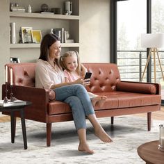 a woman and her daughter sitting on a couch looking at a cell phone in the living room