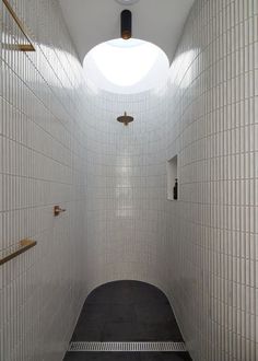 an empty white tiled bathroom with skylight in the ceiling and black floor tiles on the walls