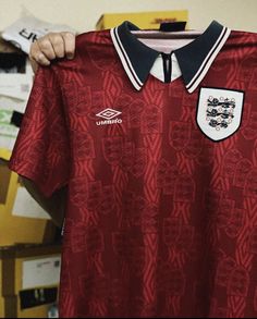 a man holding up a red shirt with white and black trims on the collar