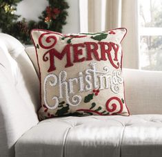 a merry christmas pillow sitting on top of a white couch next to a christmas tree