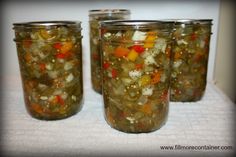 four jars filled with pickled vegetables on top of a white cloth covered tablecloth