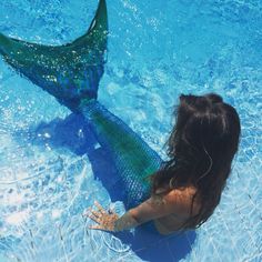 a woman is sitting in the water with a mermaid tail on her back and long black hair