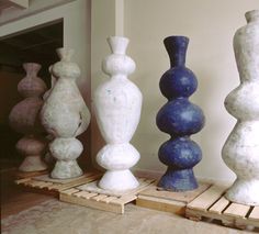 five different colored vases sitting on wooden pallets in a room with white walls