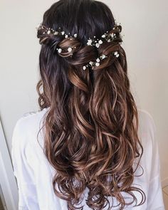 the back of a woman's head with long wavy hair and flowers in her hair