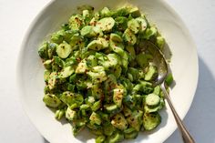 a white bowl filled with green vegetables on top of a table next to a fork