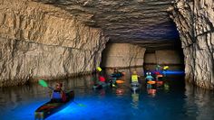 a group of people in kayaks paddling through a cave filled with blue water