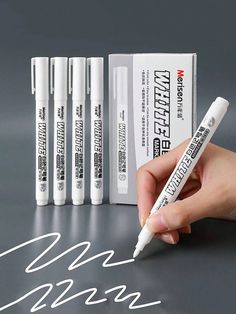 a hand is writing on a piece of paper next to four batteries and one pen