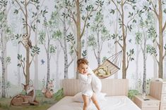 a little boy sitting on top of a bed next to a forest mural