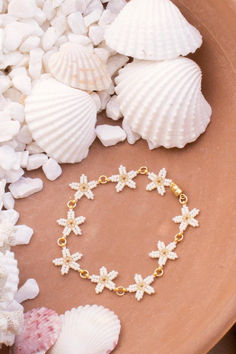 a bracelet with white flowers on it sitting next to seashells