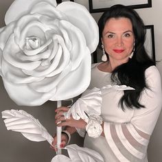 a woman holding a giant white rose in front of a wall with pictures on it