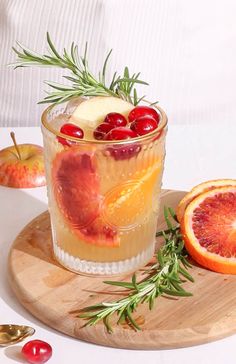 an apple cider cocktail with oranges and cranberries on a cutting board