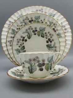 an antique tea cup and saucer with grapes on the rim, set against a gray background