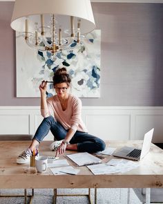 a woman sitting on the floor in front of a table with laptops and papers