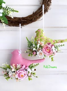 two pink hats hanging from a wreath on a white wall with flowers and greenery