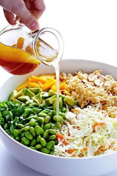 a person pouring dressing into a bowl filled with vegetables and beans, including carrots