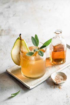 an apple cider sits on a tray next to a pitcher and spoon with some leaves in it