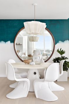 a dining room table with white chairs and a round mirror