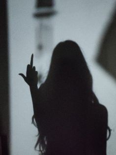 the silhouette of a woman holding her hand up in front of her face and pointing at something