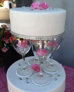 three wine glasses are sitting on top of a white cake with pink flowers in them