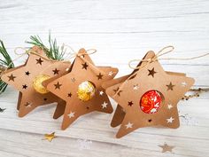 three star shaped ornaments are hanging from twine on a white wooden table with pine branches