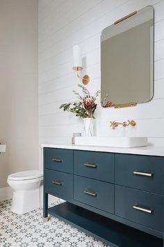 a white toilet sitting next to a blue vanity in a bathroom under a large mirror