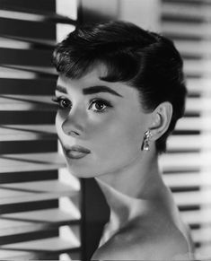 black and white photograph of a woman in front of blinds with her head tilted to the side