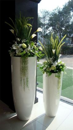 two large white vases with plants in them