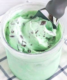 a scoop of green ice cream in a glass container with a metal spoon on top